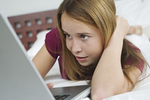 Teenage girl lying on bed, using laptop