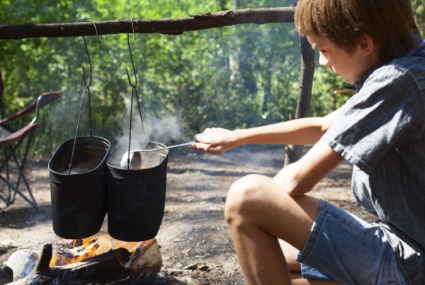 Young boy cooking camp food in cauldron on open fire